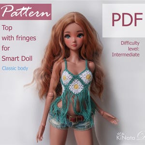 Peut inclure: Une poupée porte un haut en crochet turquoise avec des motifs de marguerites blanches et jaunes et des franges. La poupée porte un short en jean et une ceinture marron. Le texte de l'image indique "Pattern", "Top with fringes for Smart Doll Classic body", et "PDF".