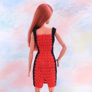 May include: A red crochet dress with black trim. The dress is sleeveless and has a fitted silhouette. The dress is shown on a doll.