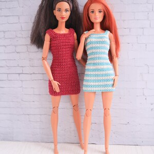 May include: Two Barbie dolls wearing crocheted dresses. One doll is wearing a red dress and the other is wearing a blue and white striped dress.