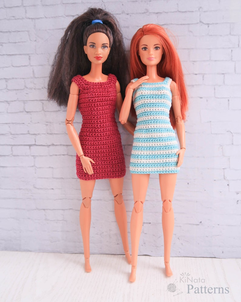May include: Two Barbie dolls wearing crocheted dresses. One doll is wearing a red dress and the other is wearing a blue and white striped dress.