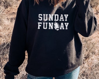 Può includere: Felpa nera con testo bianco che recita "SUNDAY FUN-DAY" con una grafica di un pallone da calcio.