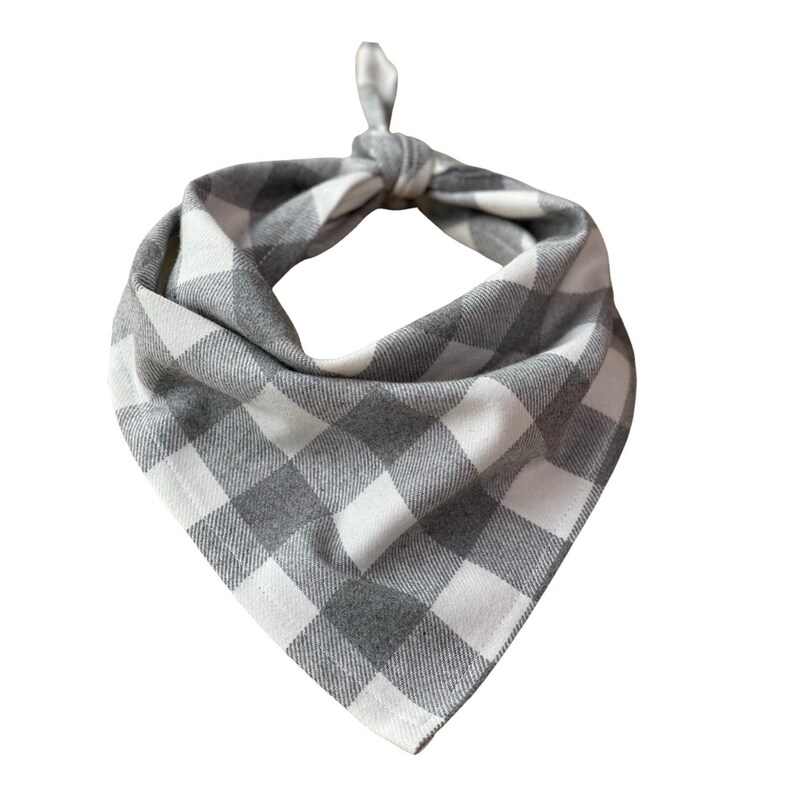 May include: A gray and white checkered dog bandana, knotted at the top. The fabric has a classic buffalo plaid pattern. The bandana is designed to be worn around a dog's neck.