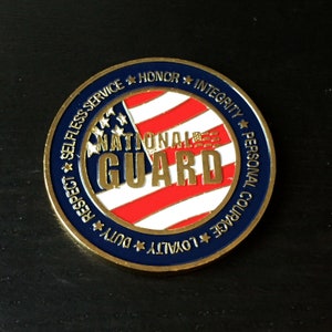 May include: Gold-colored coin with a blue and red American flag design. The words "National Guard" are in gold lettering on the flag. The words "Selfless Service", "Honor", "Integrity", "Respect", "Duty", "Loyalty", "Personal Courage" are written around the edge of the coin.