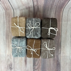 May include: Six small, rectangular packages wrapped in different shades of brown, gray, and beige felt. Each package is tied with a white string and a simple bow.