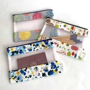 Può includere: Tre pochette con cerniera in rete con motivi diversi. La prima pochette ha uno sfondo grigio con cerchi gialli e rosa. La seconda pochette ha uno sfondo bianco con un motivo colorato di foglie, animali e bacche. La terza pochette ha uno sfondo bianco con un motivo floreale blu e giallo.