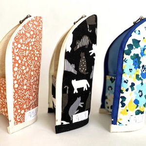 May include: Three zippered pencil cases with different fabric patterns. The first case has a white and orange floral pattern. The second case has a black and white cat pattern. The third case has a white and blue floral pattern.