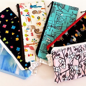 Könnte beinhalten: Fünf verschiedene Reißverschlusstaschen mit verschiedenen bunten Mustern. Die Taschen sind aus Stoff und haben einen weißen Reißverschluss. Die Muster umfassen Blumen, Vögel und geometrische Designs.