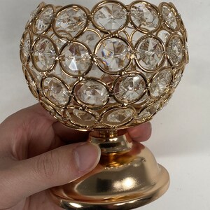 May include: Gold metal candle holder with a round, crystal-encrusted design. The holder has a wide, round base.