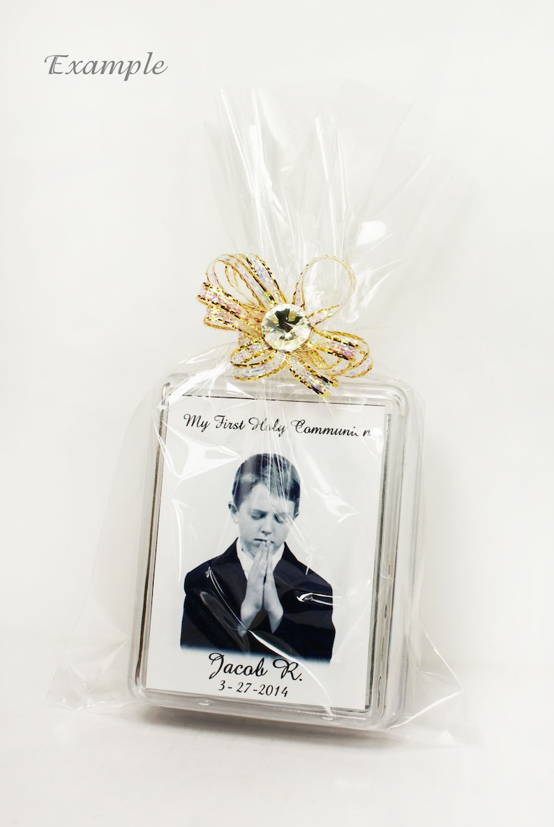 May include: A clear plastic bag with a gold ribbon and a clear plastic frame with a black and white photo of a boy in a suit praying. The frame has the text "My First Holy Communion" and "Jacob R. 3-27-2014".