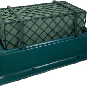 Op de afbeelding: Een groene plastic bloemsteekschuimhouder met een groene draadgaas bloemsteekschuimsteen erin. De houder heeft een rechthoekige basis en een verhoogde rand aan de bovenkant.