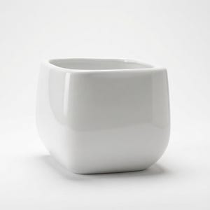 May include: A white ceramic planter with a square shape and rounded corners. The vessel features a smooth, glossy finish and a wide, open top, presenting a clean and simple design suitable for holding small plants or decorative items.