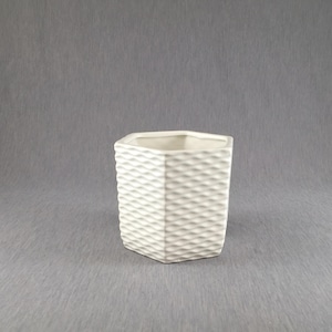 May include: A square, off-white ceramic planter with a textured, woven pattern. The planter has a hexagonal opening and is suitable for small plants or succulents. The neutral color and geometric design make it a versatile decorative item.