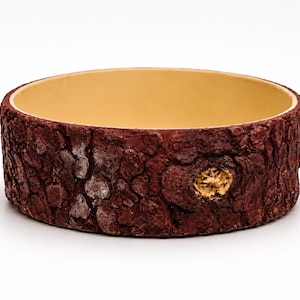 May include: A round bowl with a smooth, light beige interior and a textured exterior that mimics the appearance of dark brown tree bark, featuring a small, circular knot detail on the side with a metallic gold finish.