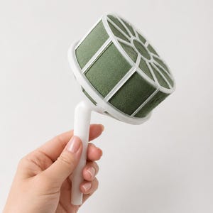 May include: A floral foam holder featuring a cylindrical block of dark green foam encased in a white plastic cage with a radial grid pattern, attached to a sturdy white plastic handle for arranging flowers in a bouquet or centerpiece.