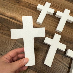 May include: Five white foam crosses of various sizes. The crosses are on a wood surface.