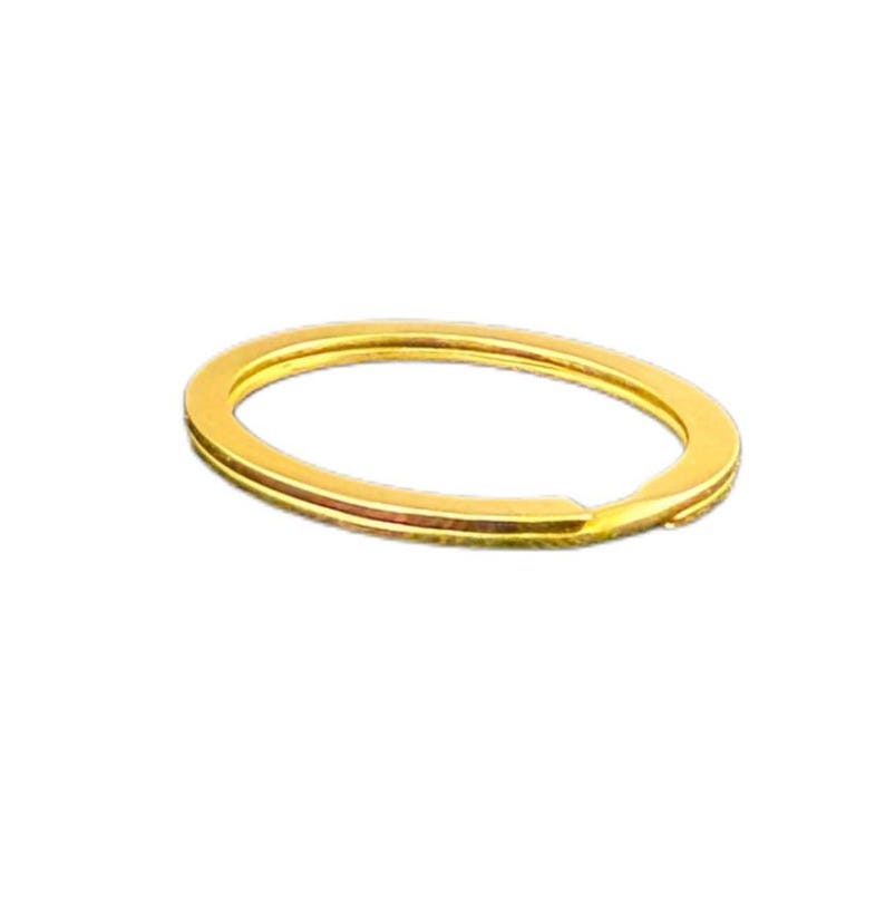 May include: A gold-colored split key ring, oval-shaped, with a small opening. The key ring is made of metal and has a shiny finish. The key ring is designed to hold keys or other small items.