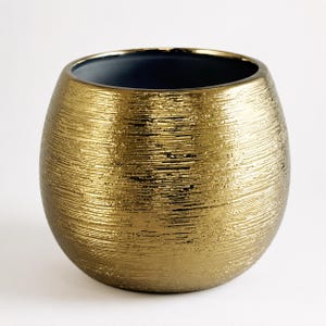 May include: A spherical planter with a metallic gold exterior featuring a horizontal, textured, brushed finish. The interior of the vessel is a smooth, dark charcoal grey, creating a contrast with the reflective, shimmering gold outer surface.