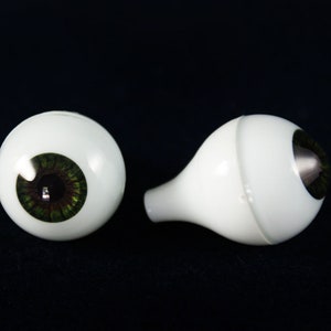 Puede incluir: Dos ojos de mu&ntilde;eca de pl&aacute;stico blanco, uno con iris verde y el otro con iris plateado.