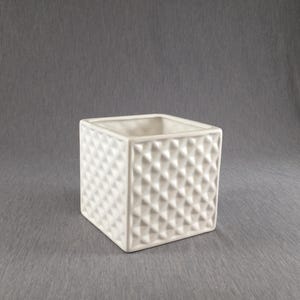 May include: A square, white ceramic planter with a textured, diamond pattern. The planter is cube-shaped and has a smooth interior. The neutral color and geometric design make it suitable for various decor styles.