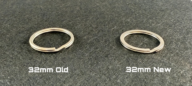May include: Two silver-colored key rings, one labeled "32mm Old" and the other "32mm New", are displayed on a dark gray surface. The key rings are circular with a split for attaching keys. The text is white.