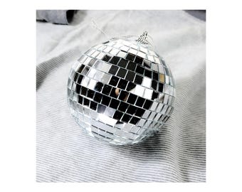 May include: A silver disco ball ornament with a mirrored surface. The ball is made up of many small squares that reflect light.
