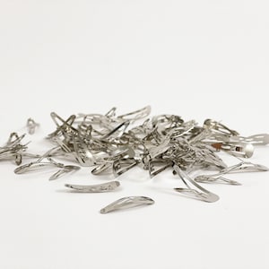 May include: A pile of silver metal hair clips. The clips are all the same size and shape, and they are arranged in a random pattern.