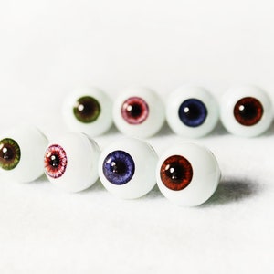 Puede incluir: Una fila de siete ojos de mu&ntilde;eca blancos con iris de diferentes colores. Los iris son verdes, rojos, rosas, azules, marrones, morados y rojos.