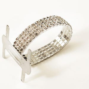 May include: A silver bracelet with a row of clear rhinestones. The bracelet has a clasp that is open.