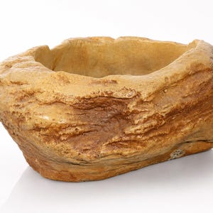 May include: A tan and brown bowl with a textured, uneven exterior that mimics the appearance of natural rock. The vessel has a wide, open top with a rough, jagged rim and a deep, hollow center, featuring organic, layered patterns throughout.