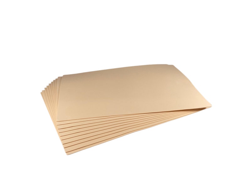 Puede incluir: Una pila de hojas de papel de color beige, probablemente cartulina o material similar, se muestra sobre un fondo blanco. Las hojas est&aacute;n cuidadosamente dispuestas, con una ligera curva visible en los bordes superiores. El papel parece nuevo y sin usar.