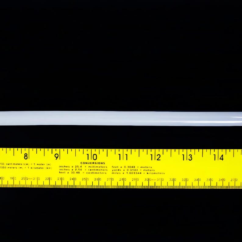 May include: A straight, translucent white cylindrical rod positioned horizontally above a yellow ruler. The ruler displays imperial measurements from 7 to 15 inches, with a conversion chart printed in the center section between 8 and 14 inches.