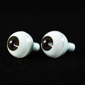 Puede incluir: Dos ojos de vidrio de aspecto realista con iris marrones y escler&oacute;ticas blancas. Los ojos est&aacute;n montados en bases de pl&aacute;stico blanco con un peque&ntilde;o agujero para la fijaci&oacute;n.