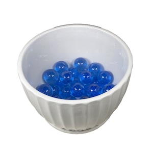 May include: A white ceramic bowl with a fluted rim filled with blue glass marbles.