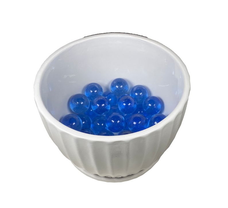 May include: A white ceramic bowl with a fluted rim filled with blue glass marbles.