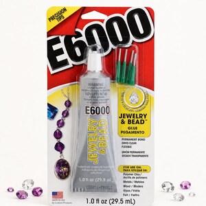 Puede incluir: Un tubo de 29,5 ml de adhesivo E6000 Jewelry & Bead en su empaque original. El tubo plateado incluye cuatro puntas de precisi&oacute;n verdes. La tarjeta roja y amarilla presenta texto, un gr&aacute;fico de un collar de cuentas moradas y cristales.