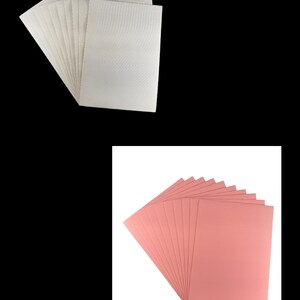 May include: Two stacks of corrugated cardboard sheets. One stack is white and the other is pink.