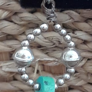 May include: Silver bead and turquoise charm dangle earrings. The earrings feature a circle of silver beads with two larger silver beads on either side of a turquoise charm.