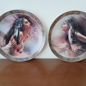 May include: Two decorative ceramic plates with a marbled background and gold trim. Each plate features a painting of a woman with long flowing hair and a feather headdress. The woman on the left is holding a feather in her hand, while the woman on the right is looking up with her hand on her chest.