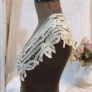 May include: Ivory lace collar with a scalloped edge, displayed on a brown mannequin. The delicate openwork design is visible, showcasing the intricate details of the vintage textile. The collar is a vintage item.