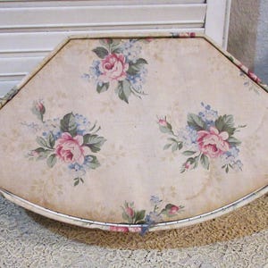 May include: A vintage, fan-shaped decorative tray with a floral pattern. The tray features a cream-colored background adorned with pink roses and blue accents. The tray has a metal trim and is placed on a lace surface.