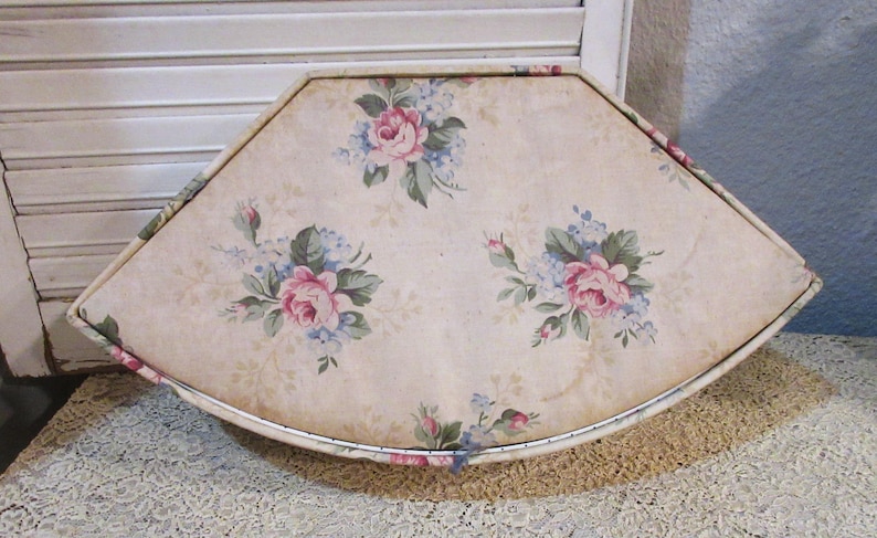 May include: A vintage, fan-shaped decorative tray with a floral pattern. The tray features a cream-colored background adorned with pink roses and blue accents. The tray has a metal trim and is placed on a lace surface.