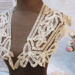 May include: Ivory lace bolero with a delicate openwork design. The bolero features short sleeves and scalloped edges. The intricate lace pattern is visible, showcasing the garment's craftsmanship. This vintage-inspired piece adds a touch of elegance.