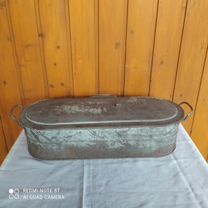 Könnte beinhalten: Ein vintage, ovaler Metallbehälter mit Deckel und zwei Griffen. Der Behälter ist aus verzinktem Metall und hat ein rustikales, verwittertes Aussehen.