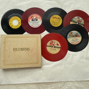 May include: A collection of vintage 45 RPM records, featuring black and red vinyl discs. The records are from Peter Pan Records and are accompanied by a beige record storage box labeled "RECORDS". The labels display colorful illustrations.