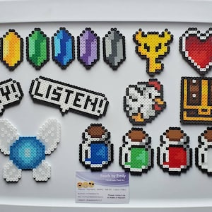 Peut inclure: Une collection de 14 motifs d'art pixelisés réalisés avec des perles Perler colorées. Les motifs comprennent un cœur, un coffre, un poulet, une clé, un ensemble de six gemmes, deux bulles de dialogue qui disent "HEY!" et "LISTEN!" et quatre fioles de potion.
