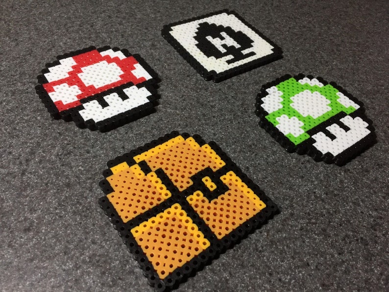 May include: Four pixel art designs made with colorful beads. The designs include a red and white mushroom, a green and white mushroom, a yellow and orange brick block, and a white and black block with a question mark.