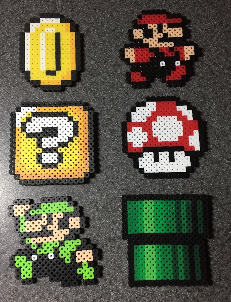 May include: A set of six pixel art characters from the Super Mario Bros. video game series. The characters are made of colorful plastic beads and include Mario, Luigi, a mushroom, a coin, a question block, and a green pipe.