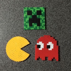 May include: Three pixel art coasters featuring a green creeper face, a red Pac-Man ghost, and a yellow Pac-Man.