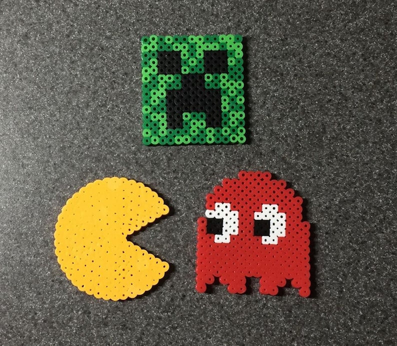 May include: Three pixel art coasters featuring a green creeper face, a red Pac-Man ghost, and a yellow Pac-Man.