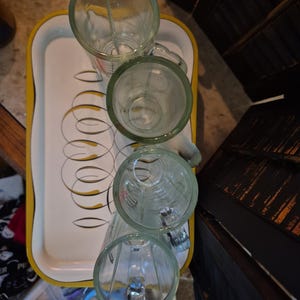 Puede incluir: Cuatro tazas de vidrio transparente con asas est&aacute;n dispuestas sobre una bandeja blanca con un borde amarillo y un dise&ntilde;o retro. Las tazas tienen un borde verde. La bandeja est&aacute; sobre una superficie con otros elementos en el fondo.